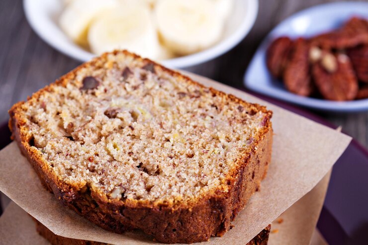 Freshly baked banana bread loaf sliced on a wooden cutting board, garnished with bananas and walnuts.